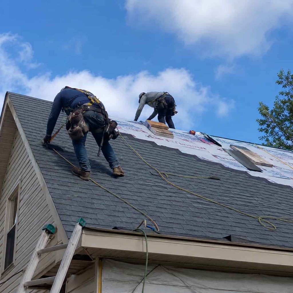 Professional roof installation in progress with roofing contractors installing asphalt shingles on a residential home roof.