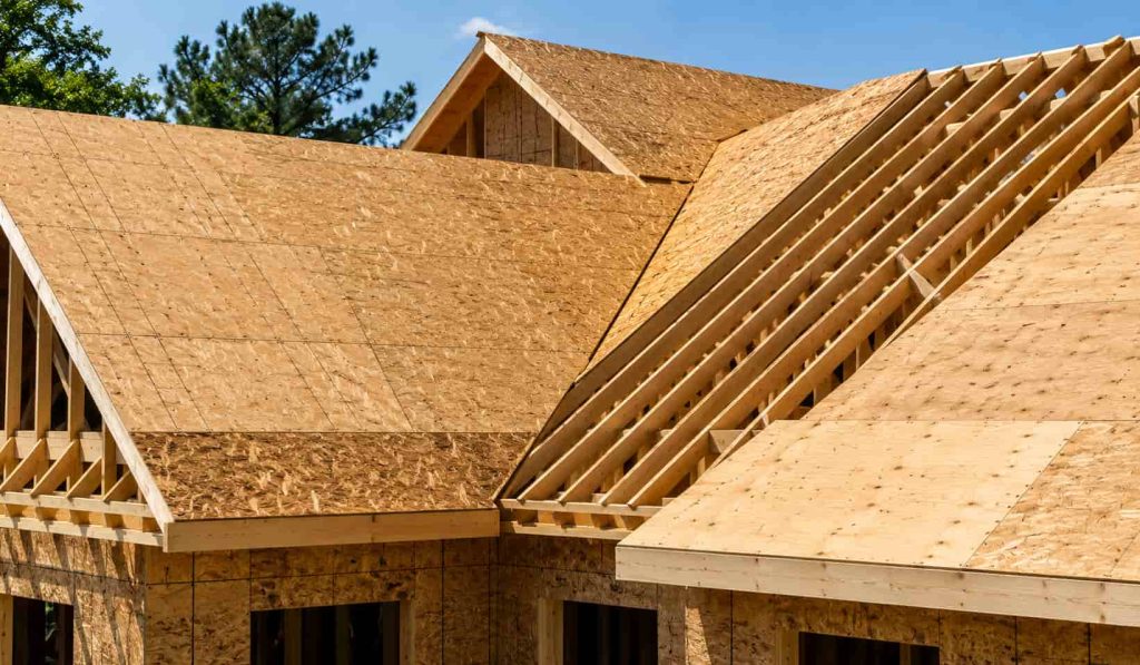 Residential roof decking installation showing exposed OSB and plywood sheathing over wooden rafters on a partially constructed home, highlighting roof structure and decking materials in bright daylight.