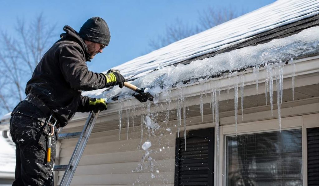 Professional worker performing ice dam removal on a snow-covered residential roof in NYC.