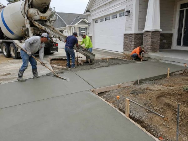 Professional concrete installation project featuring a newly poured and finished concrete driveway in front of a residential property, with contractors leveling and smoothing the surface for a durable, long-lasting finish. concrete work