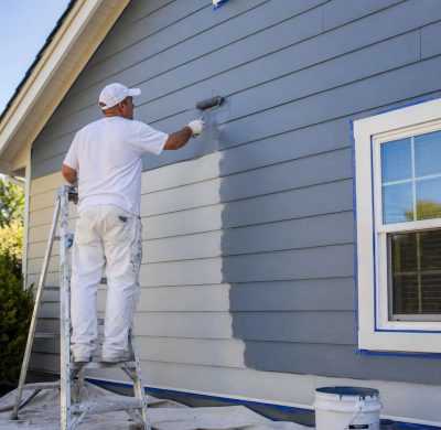 Professional contractor painting exterior house siding with weather-resistant coating during a residential siding improvement project.